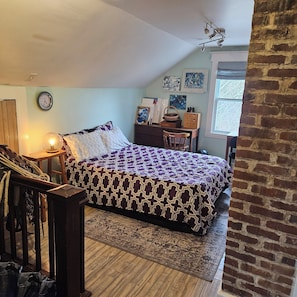 A bedroom with a bed, a desk, a chair, a clock, and artwork on the walls. - Camp Nova a Cozy Cedar-clad Cottage in Scenic Tangier, Canada (Tangier)