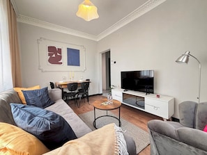 Ein modernes Wohnzimmer mit Sofa, Sessel, Couchtisch und Fernseher.
