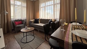 A modern living room with a sofa, a coffee table, a dining table with candles, and large windows with sheer curtains. - Unique 1BR w/ Hammam • Near Şişhane - Galata (Istanbul)