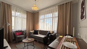 Ein modernes Wohnzimmer mit Sofa, Couchtisch, Esstisch und Vorhängen.
