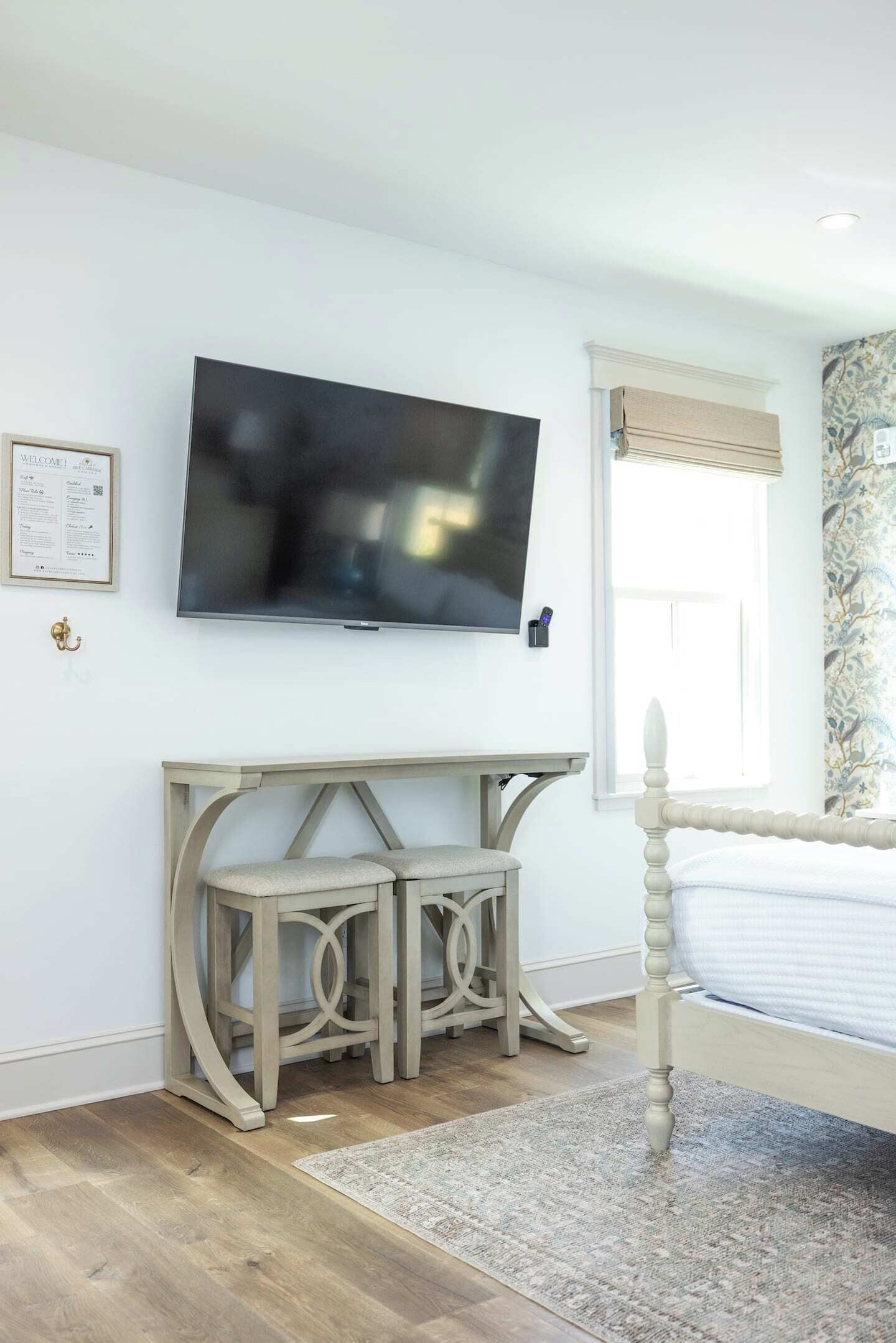 Un dormitorio con cama, televisor en la pared, escritorio con silla y ventana con cortinas.