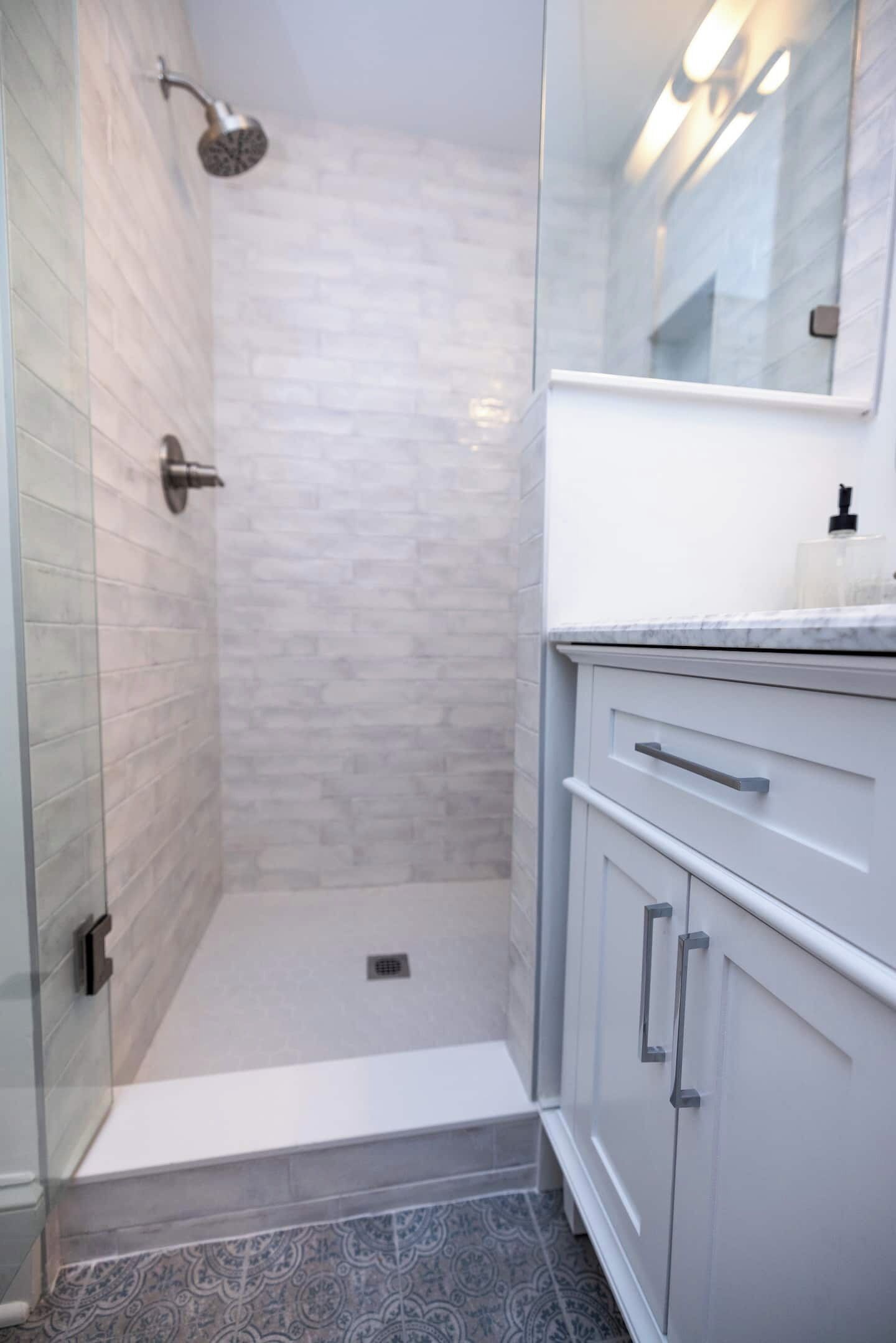A bathroom with a shower, tiled walls, a sink, and a mirror.