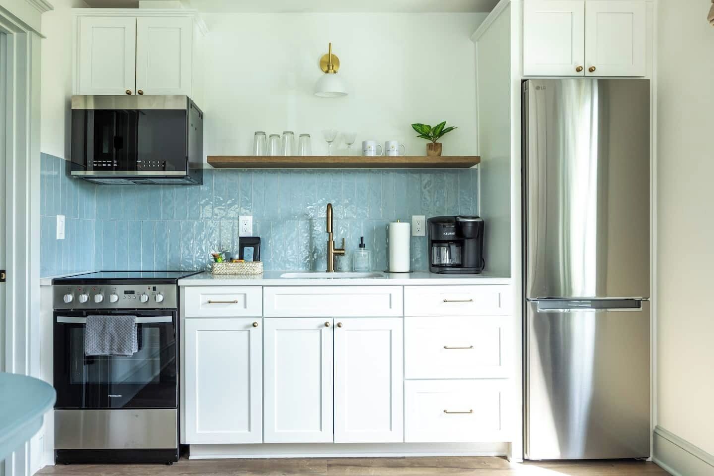Una cocina con armarios blancos, un refrigerador de acero inoxidable, una cafetera y un microondas.