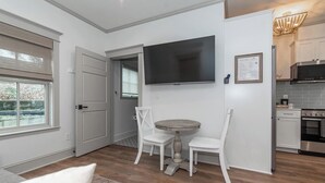 Eine moderne Küche mit Flachbildfernseher, weißen Schränken und einem Essbereich mit rundem Tisch und zwei Stühlen.