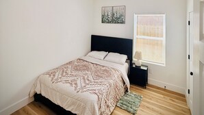 Et soveværelse med en seng, et natbord, et vindue med rullegardiner og en loftlampe.