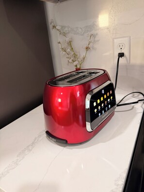 Ein roter Toaster auf einer weißen Arbeitsplatte, mit einer Steckdose und einem Blumenvasen im Hintergrund.