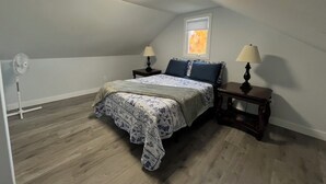 Une chambre à coucher avec un lit, deux tables de chevet, une fenêtre et un ventilateur de plafond.