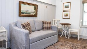 A living room with a grey sofa, two plaid cushions, a small round table, a white chair, and a framed picture on the wall.