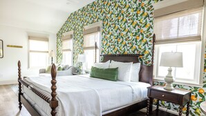 A bedroom with a four-poster bed, a nightstand with a lamp, and a wall with a fruit pattern. - Luxury Boutique Hotel | All 8 Suites | Sleeps 24 | Steps from St. George Street! (St. Augustine)