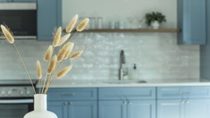 A kitchen with blue cabinets, a white vase with dried wheat stalks, and a white tiled backsplash. - Luxury Boutique Hotel | All 8 Suites | Sleeps 24 | Steps from St. George Street! (St. Augustine)