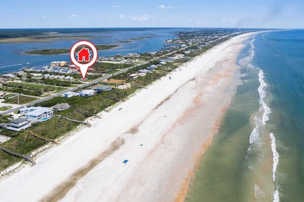 Vista aérea de una zona costera con playa, casas y un puerto deportivo.