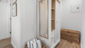 Ein weißes Zimmer mit Holztür, einem Spiegel, einem Korbwannen und gerahmten Bildern an der Wand.