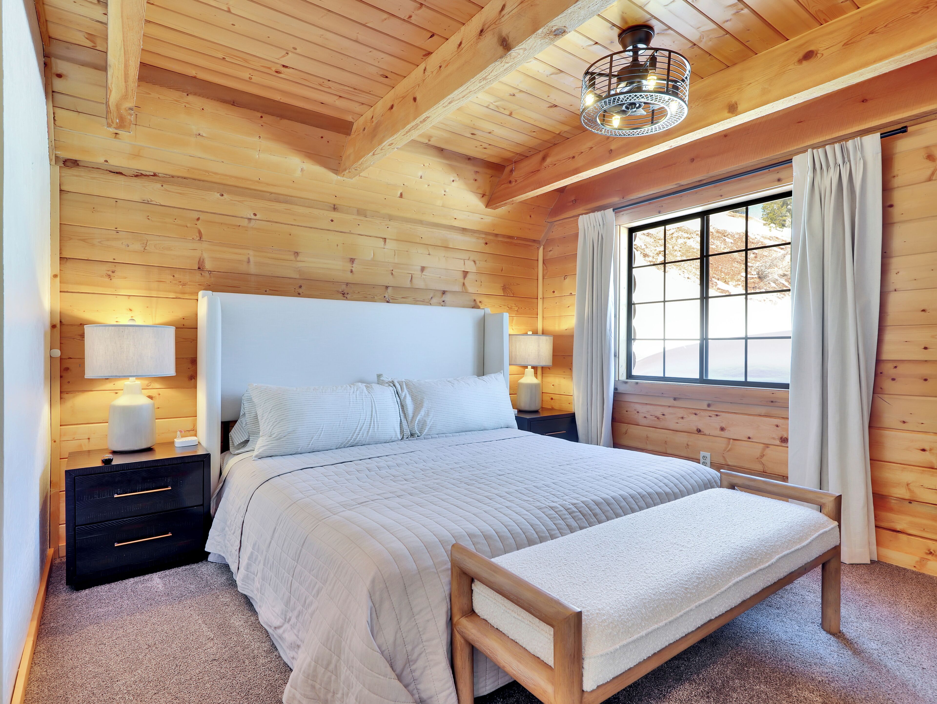 Une chambre dans une cabane en bois, avec un lit, des lampes de chevet, une fenêtre avec des rideaux et un plafond en bois.
