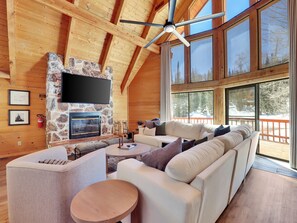 A log cabin interior with a stone fireplace, a large TV, and a cozy seating area.