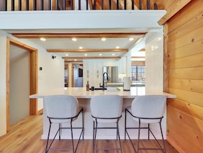 A modern kitchen with a central island, bar stools, and wooden paneling. - Fall in Brian Head means golden aspens, crisp mountain air & quieter trails. This 5-bedroom retreat pairs outdoor adventure with a hot tub, fire pit, chef’s kitchen, game room and restorative spaces for families, friends and multi-generational stay. (Brian Head)