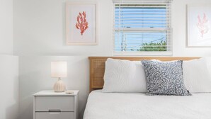 Ein ordentlich eingerichtetes Schlafzimmer mit einem Bett, einem Nachttisch, einer Lampe und zwei gerahmten Kunstwerken an der Wand.