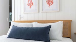 Ein Bett mit weißen und blauen Kissen, einem hölzernen Kopfteil und zwei gerahmten Korallenbildern an der Wand.