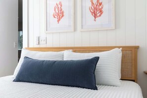 Ein Bett mit weißen und blauen Kissen, einem hölzernen Kopfteil und zwei gerahmten Korallenbildern an der Wand.