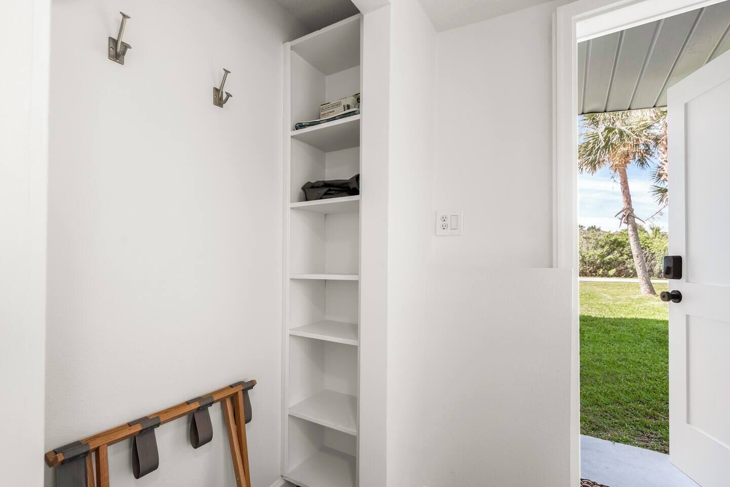 A white interior with a wooden bench, a white door leading outside, and a white wall with a shelf unit.