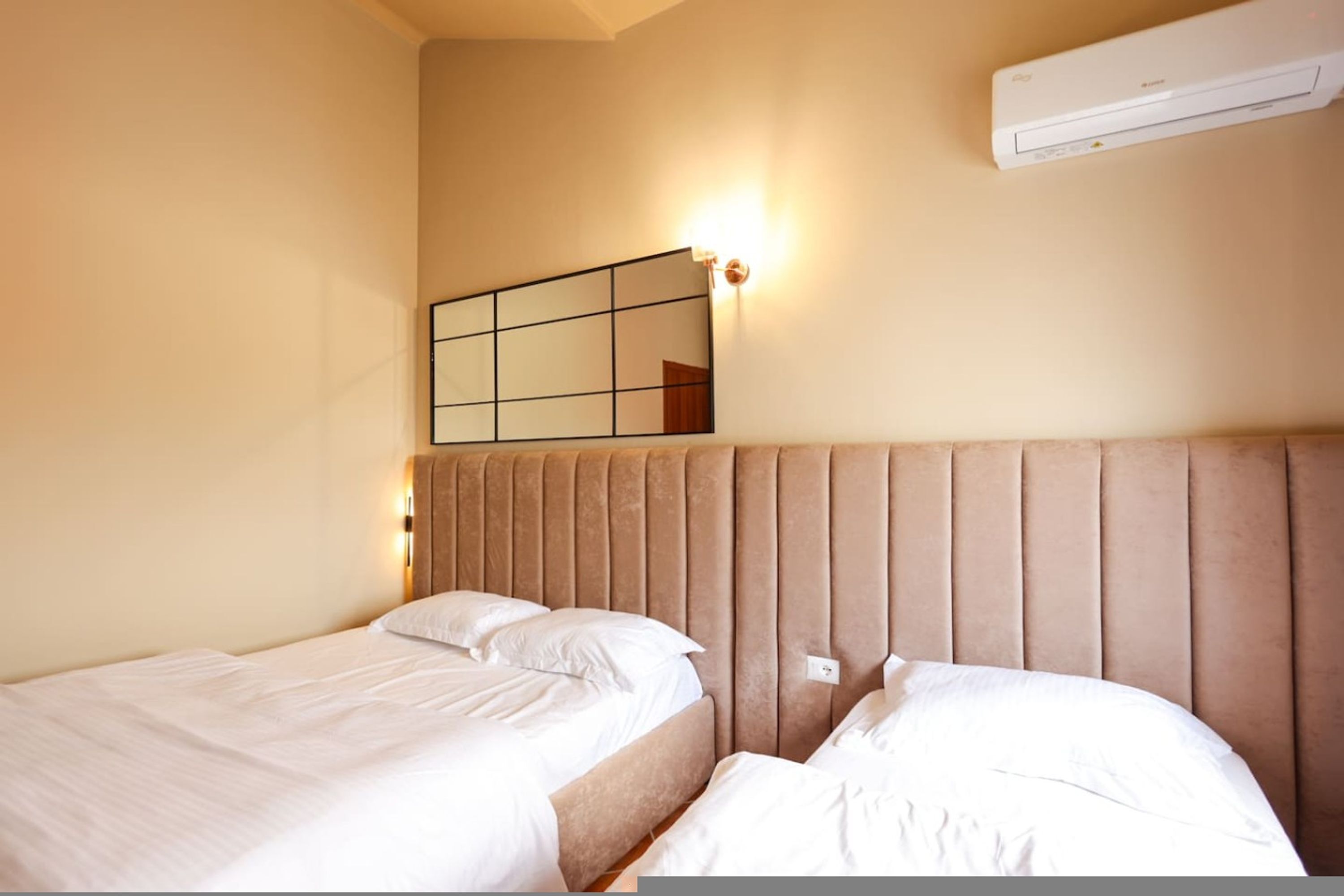 A hotel room with two beds, a wall-mounted air conditioner, and a mirror with a light.