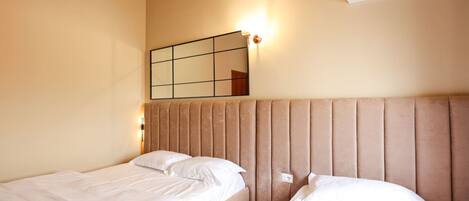 A hotel room with two beds, a wall-mounted air conditioner, and a mirror with a light.
