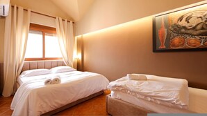 Quarto de hotel com duas camas, uma janela com cortinas, um quadro na parede e um termostato.