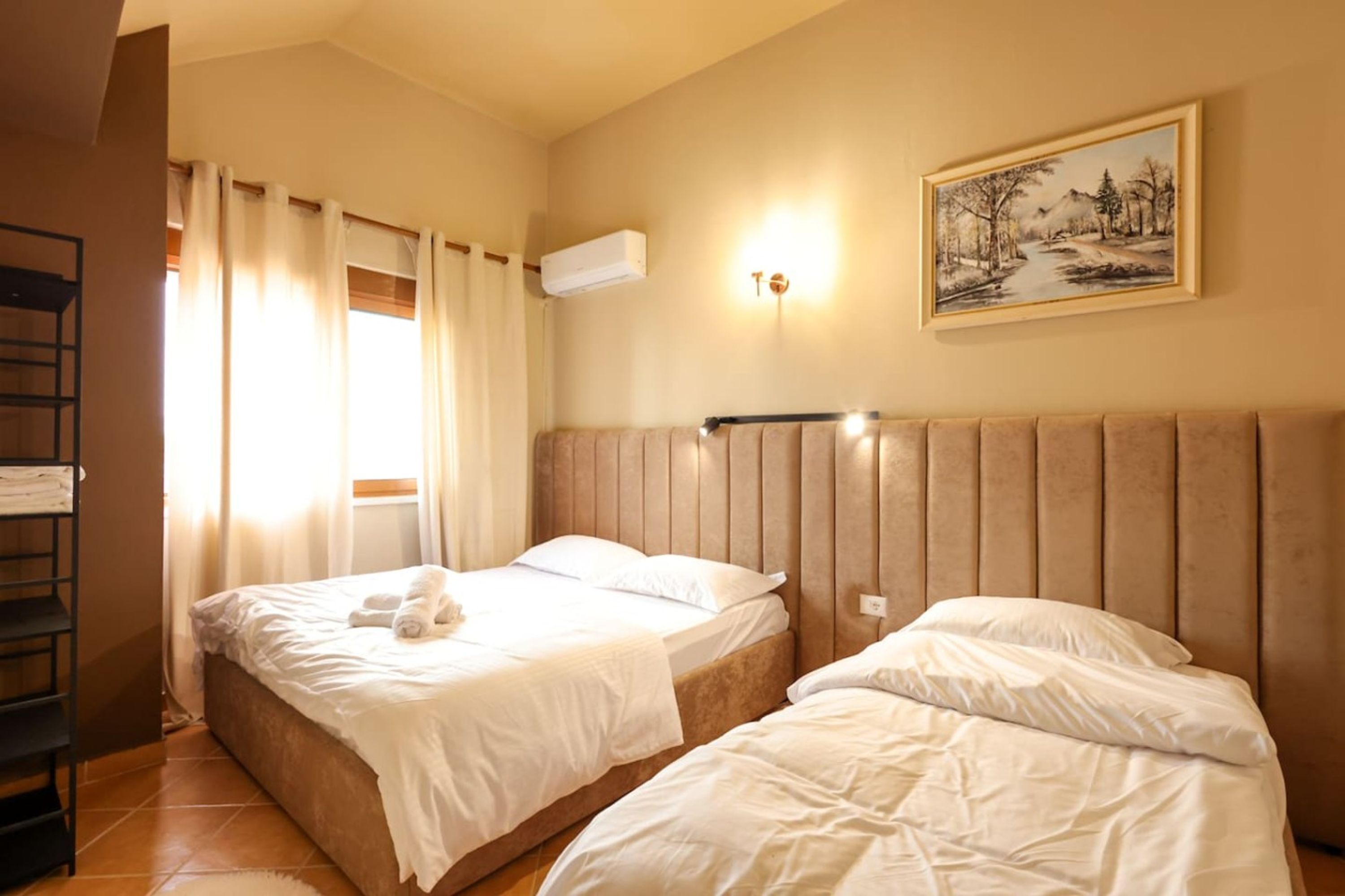 Een hotelkamer met twee bedden, een schilderij aan de muur, een airconditioning en een raam met gordijnen.