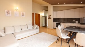 Un salon moderne avec un canapé, des fauteuils, une table à manger et une cuisine en arrière-plan.