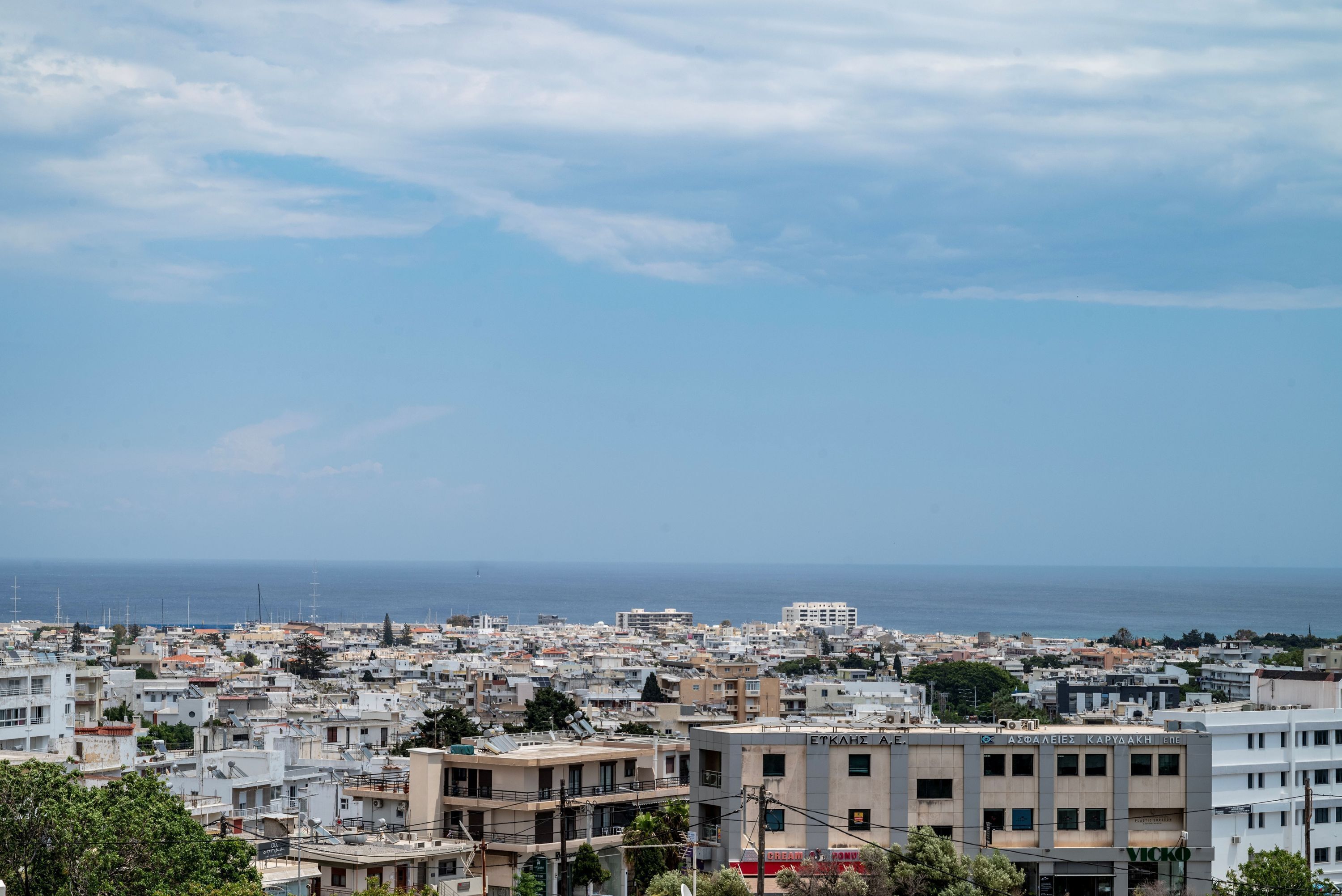 Un paysage urbain côtier avec des bâtiments, un ciel dégagé et la mer à l’horizon.