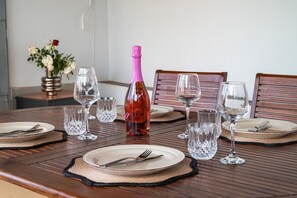 A dining table set with plates, cutlery, and wine glasses, with a bottle of wine and a vase of flowers in the background. - Hilltop Apartment in Monte Smith Rhodes (Rodos)