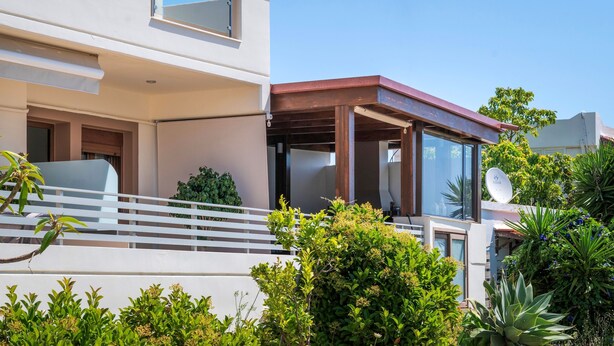 Ein modernes, zweistöckiges Haus mit Balkon, Satellitenschüssel und üppiger Bepflanzung.