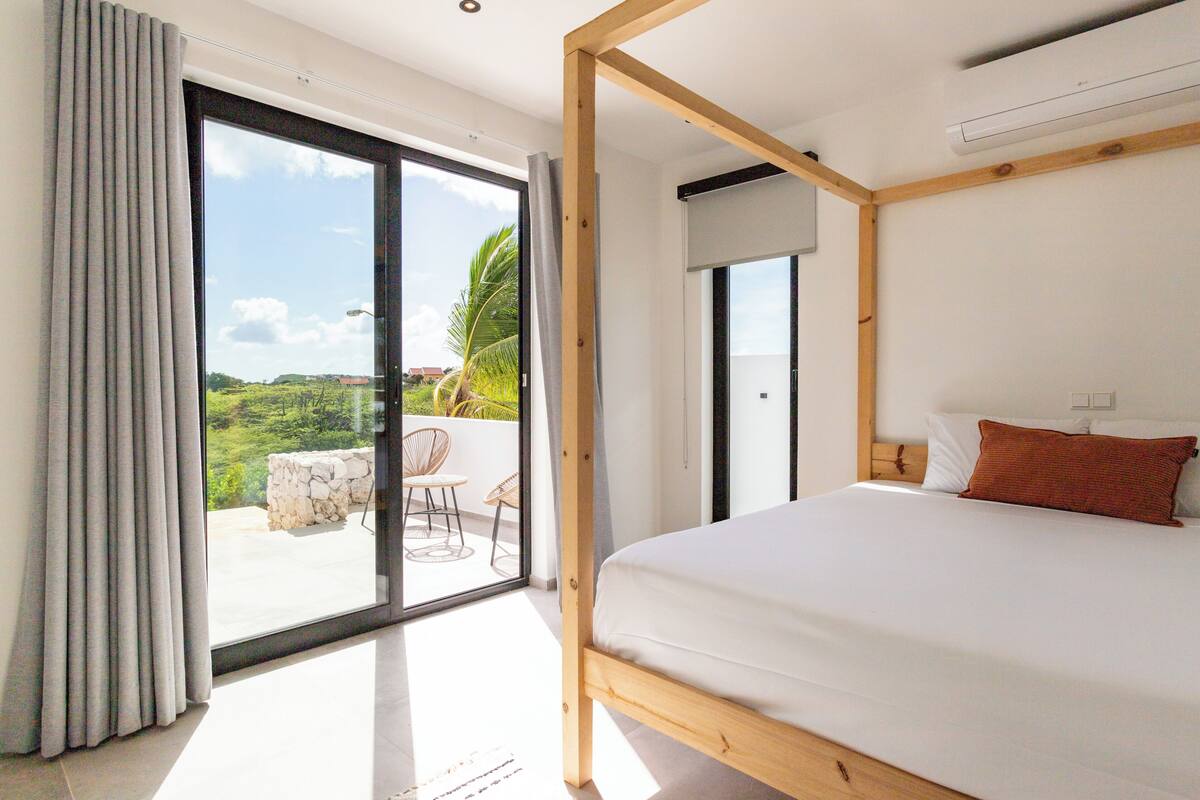 A bedroom with a large bed, a wooden headboard, a sliding glass door to a balcony, and a ceiling fan.