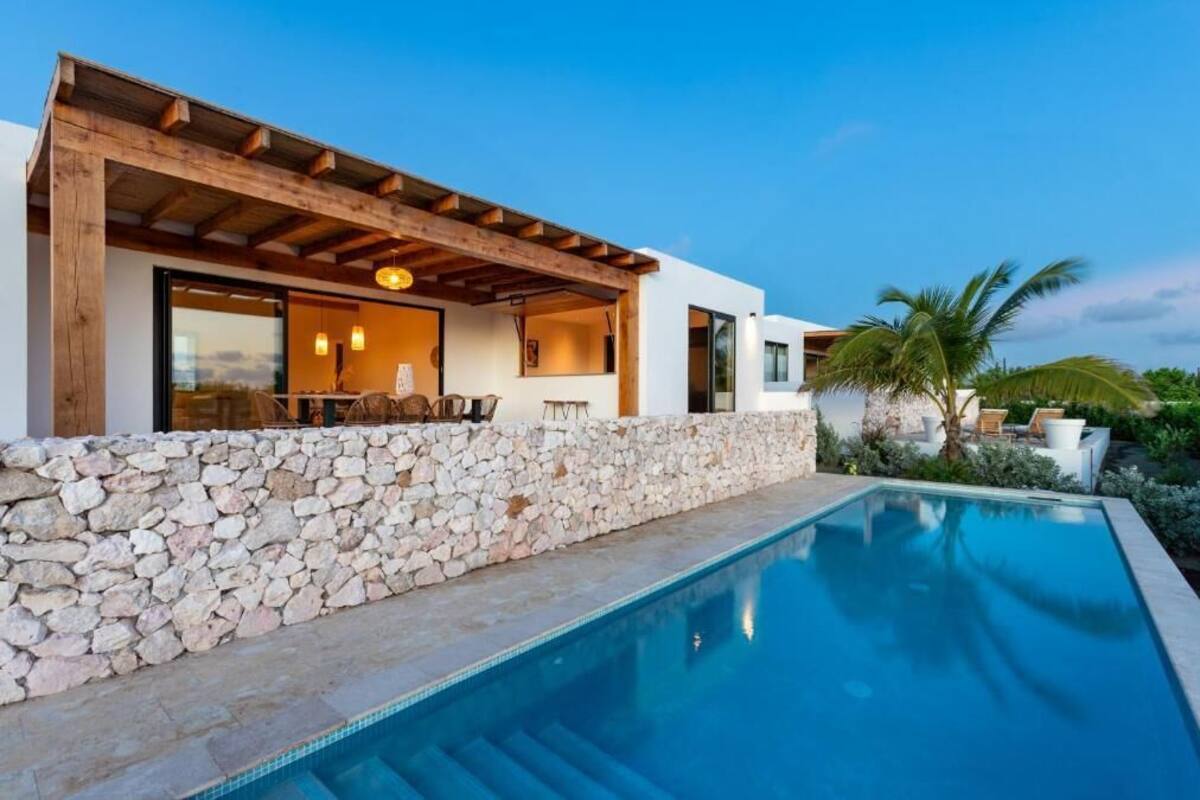 A modern house with a stone wall, a pool, and a covered outdoor seating area.