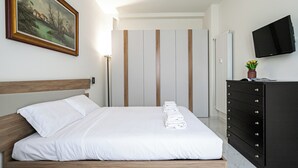 A neatly made bed with white linens, a wooden headboard, a painting on the wall, a dresser with drawers, and a television mounted on the wall. - Italianway Comfort - Mezzofanti 9 (Milan)