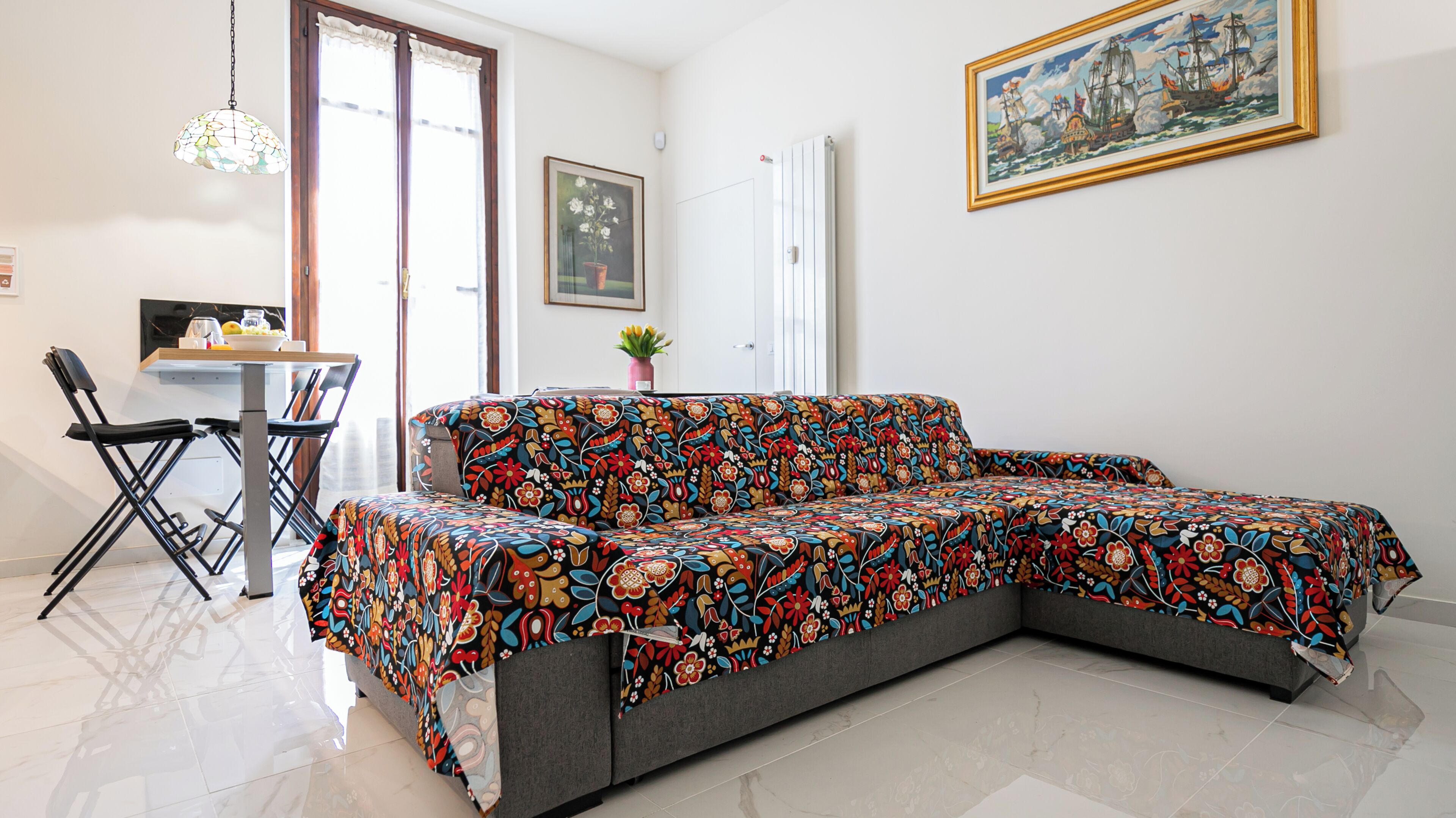 A modern living room with a sofa, a dining table, chairs, a potted plant, and a framed painting on the wall.