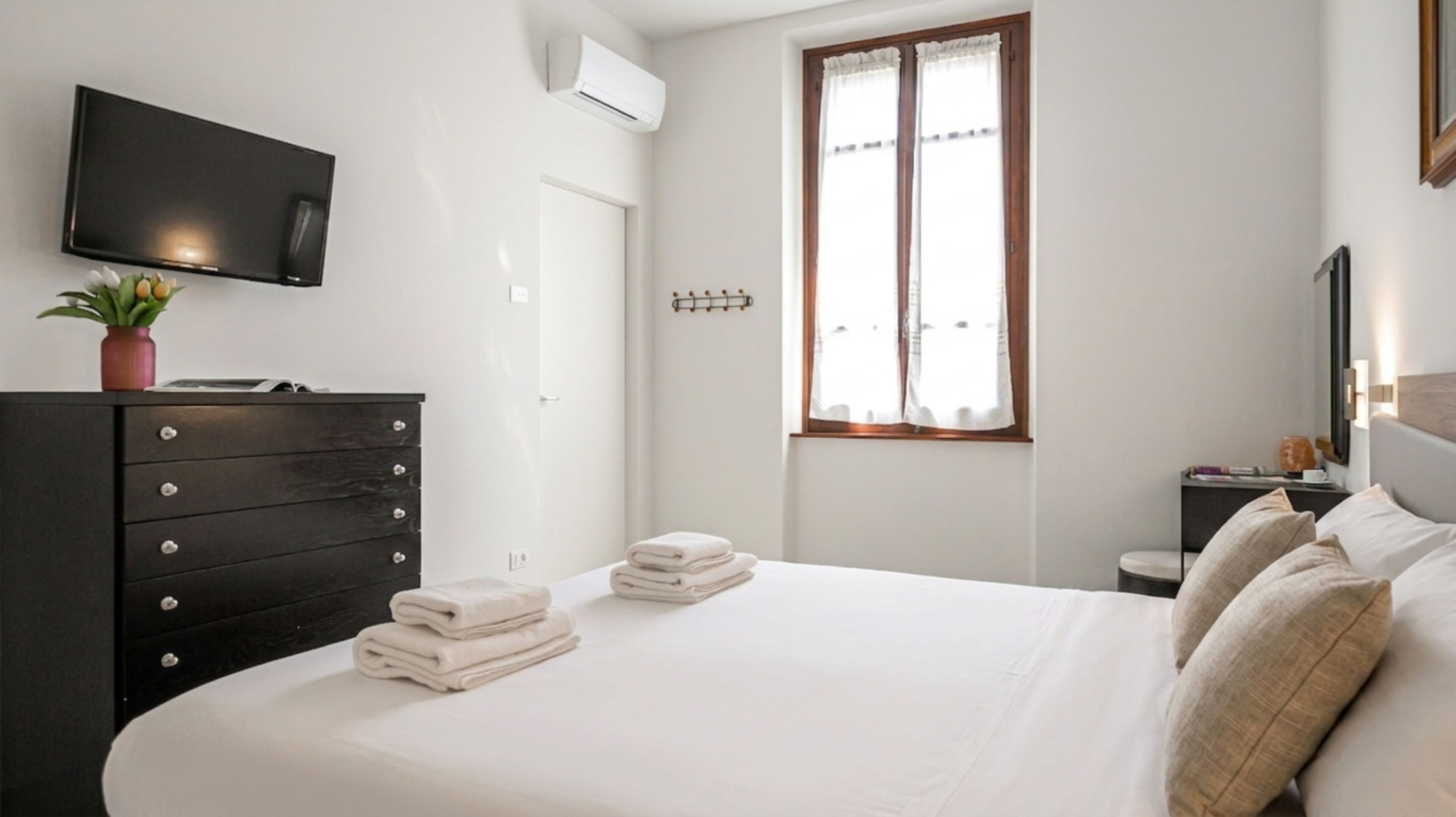 Une chambre à coucher comprenant un lit, une commode, un téléviseur, une fenêtre et une table de chevet.