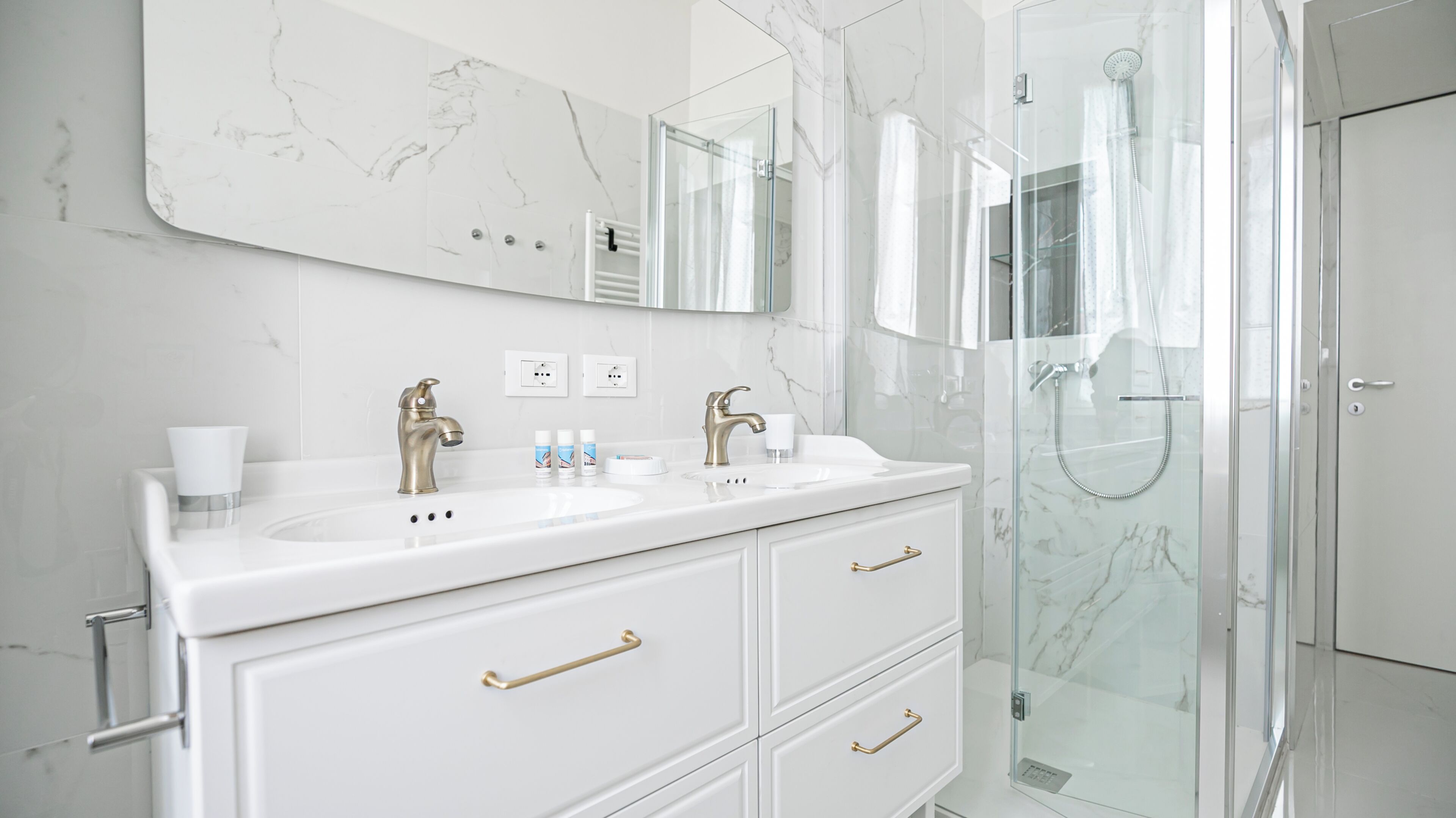 A modern bathroom with a white marble vanity, a glass shower enclosure, and a large mirror.
