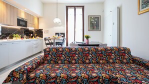 A modern kitchen with white cabinets, a built-in oven, and a dining area with a table and chairs. - Italianway Comfort - Mezzofanti 9 (Milan)