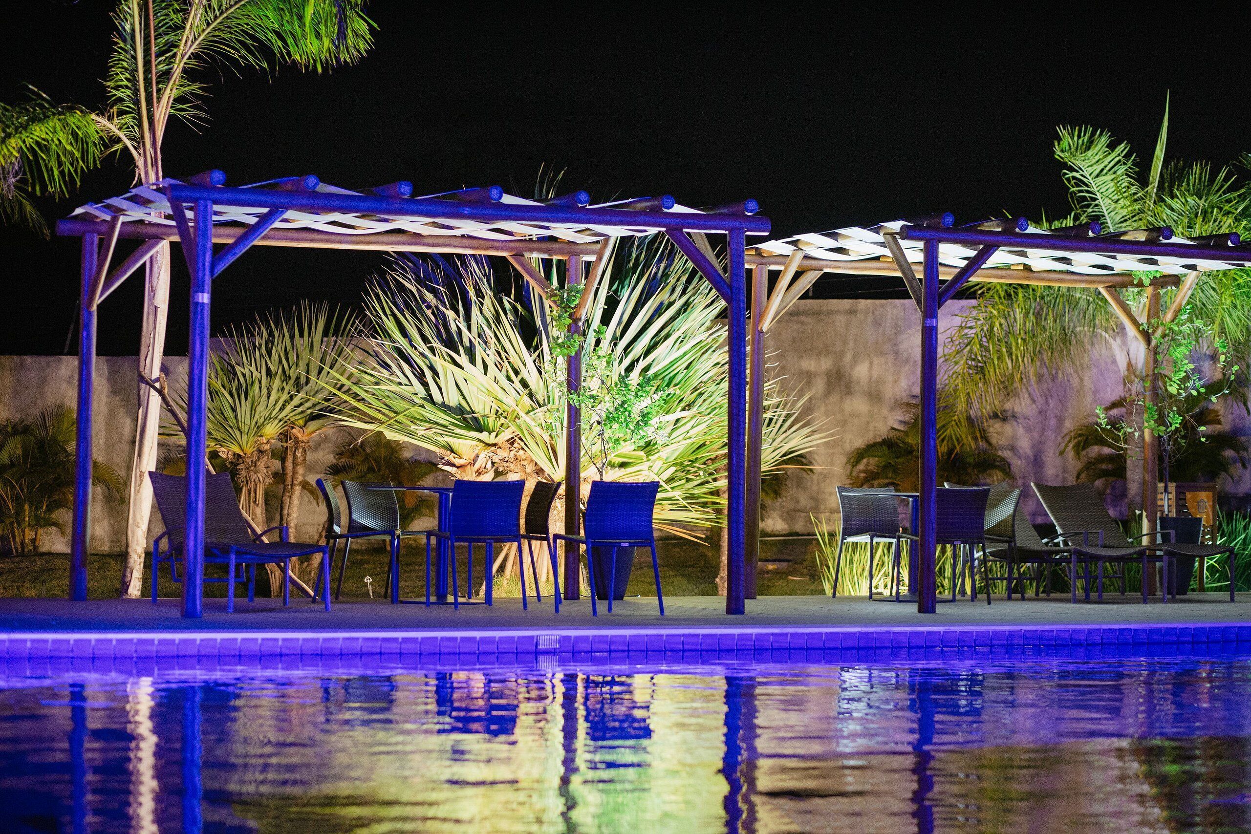 A nighttime pool area with a covered seating area and chairs.
