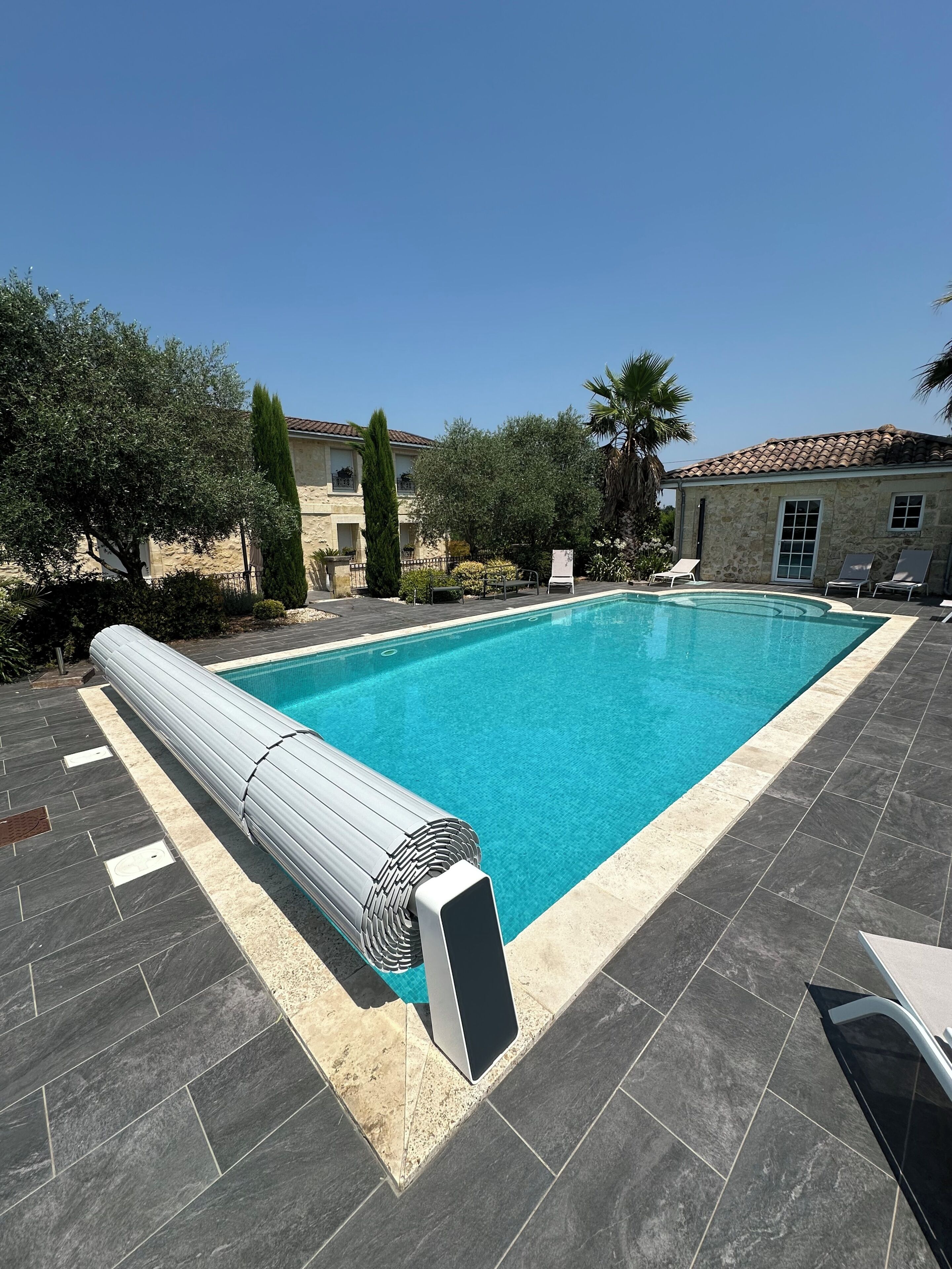 A swimming pool with a tiled deck, lounge chairs, and a stone building in the background.