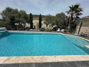 A swimming pool with lounge chairs, surrounded by trees and a stone building. - Splendid contemporary villa amidst vineyards on the outskirts of Bordeaux (saint louis de montferrand)