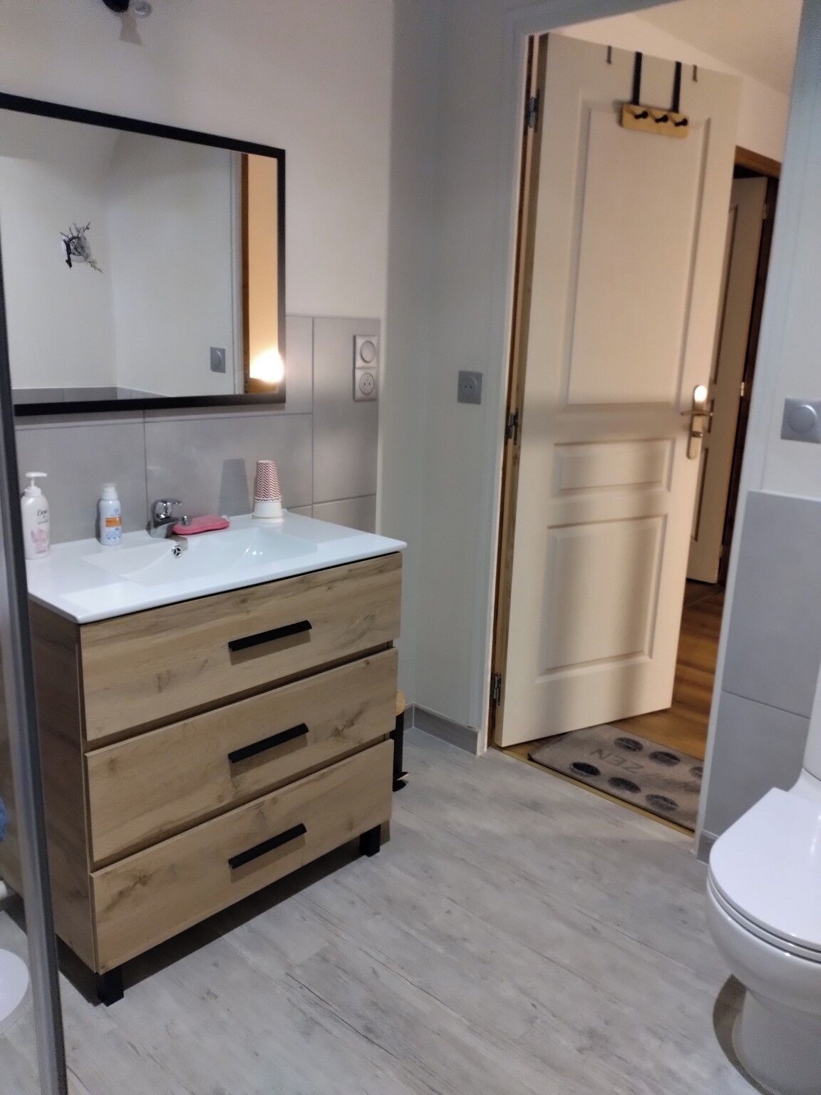 Een badkamer met een witte wastafel, houten wastafelmeubel en een spiegel.