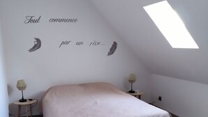 Ein Schlafzimmer mit schräg verlaufender Decke, einem Bett, zwei Nachttischen mit Lampen und einem Oberlicht.