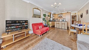 Een woonkamer met een televisie, rode bank, houten tv-meubel en een eethoek met een tafel voor vier personen.