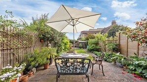 Een terras met een tafel en stoelen, omgeven door potplanten en een houten omheining.