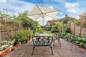 Eine Terrasse mit Tisch und Stühlen, umgeben von Kübelpflanzen und einem Holzzaun.
