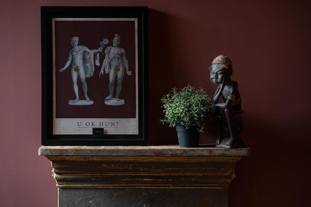 Una obra de arte enmarcada con figuras clásicas, una planta pequeña en maceta y una estatua sobre una repisa.