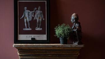 Una obra de arte enmarcada con figuras clásicas, una planta pequeña en maceta y una estatua sobre una repisa.