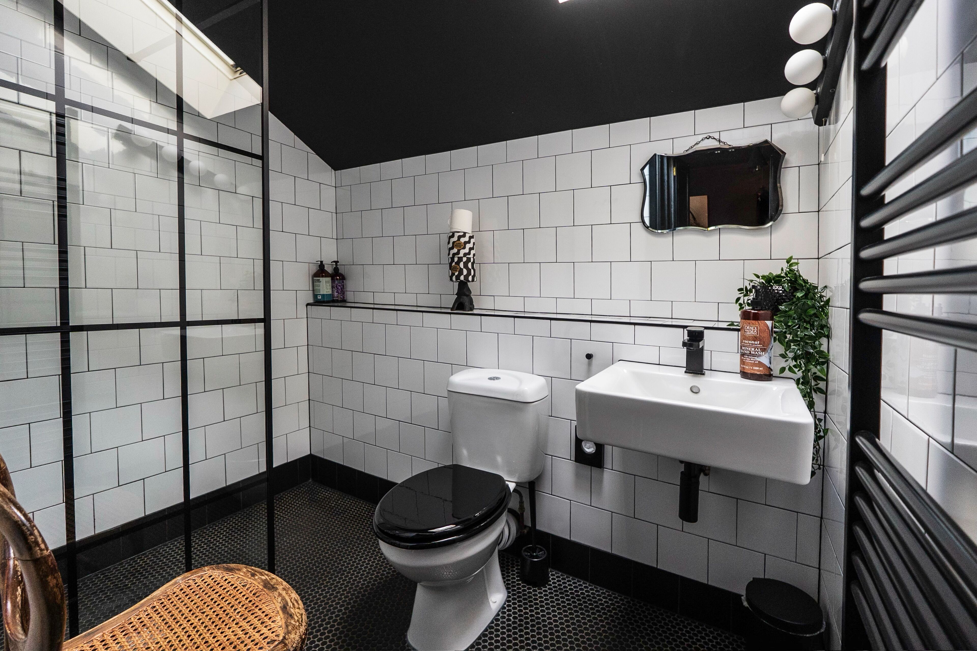 A modern bathroom with white tiled walls, a black toilet, a white sink, and a mirror above the sink.