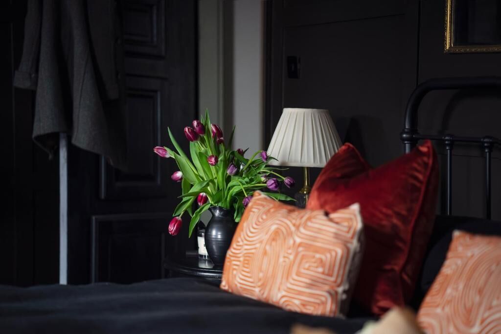 A bed with pillows, a vase with flowers, and a lamp on a bedside table.